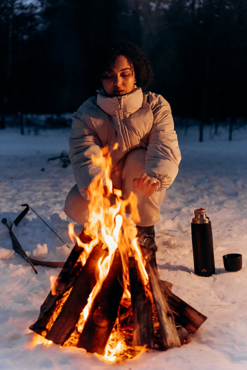 women in bubble jacket keeping herself warm beside a bonfire
